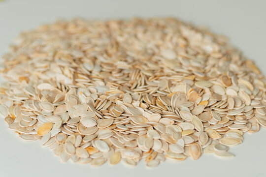 Pumpkin Seeds Scattered On White Surface. Food Ingredient Background With Copy Space.