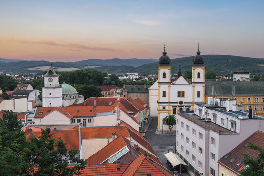 Evening cityscape of Trenc&iacute;n with Piarist Church of St. Francis Xavier, City Tower, red rooftops and hills under pastel sunset sky. Historic Slovak town