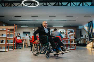 Obraz premium A smiling man in a wheelchair works in a modern open-office space with colleagues in the background.
