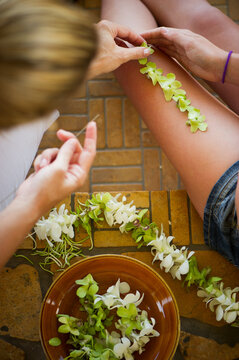 girls hands and legs arranging flowers for leis in hawaii, closeup