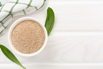 Psyllium husk powder with fresh leaves on wooden background, top view