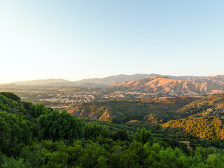 Obraz premium Green forest hills meeting dry desert mountains at sunset in warm golden light panoramic landscape photograph.