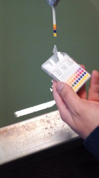 Industrial pH measurement process using test strip for chemical bath quality control in manufacturing facility, close-up inspection of liquid solution during industrial production line monitoring.