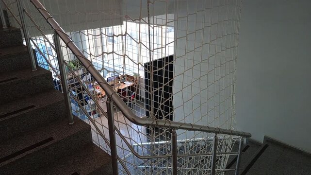 Industrial stairwell safety net installation to prevent falls, protective mesh barrier covering stair railing for workplace safety compliance in manufacturing facility.