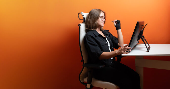 Thoughtful designer with a stylus works on a graphics tablet. The architect works on a graphic tablet on an orange background.