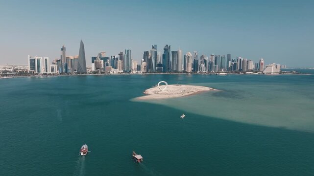 Aerial shot of the Doha skyline with traditional wooden dhows sailing across the turquoise waters of the bay on a sunny day in Qatar