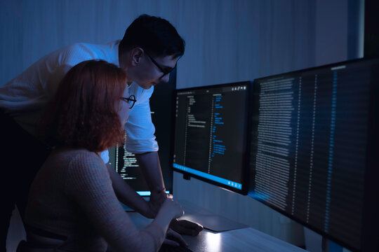 Two software developers collaborating at night, focusing on code review and debugging process on a computer screen, representing teamwork, innovation, and modern software development workflow.