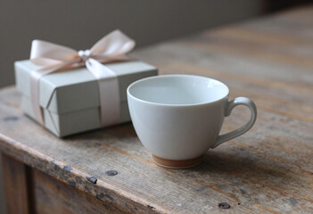 Fototapeta premium delicate ceramic cup gift box sits atop weathered wooden surface bathed soft diffused natural light