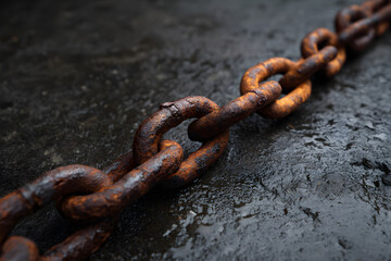 Fototapeta premium Close-up of a heavy rusty iron chain lying on a wet dark asphalt background, symbolizing strength, decay, and industrial history.