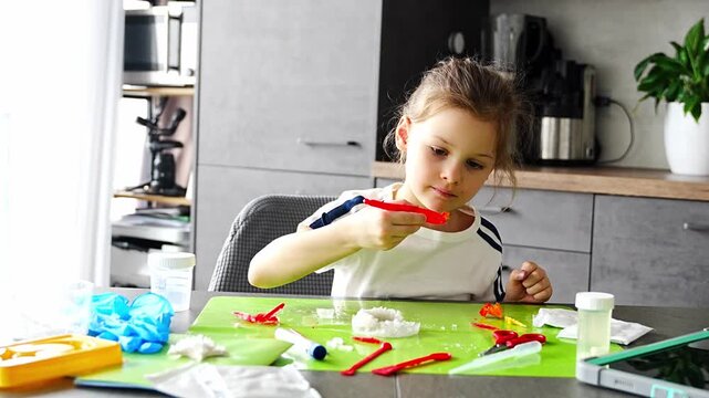 Young girl carefully holding grown crystal with tweezers and examining it during home science experiment. Precision work and analytical thinking in early STEM education and chemistry learning.