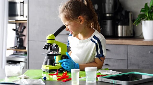 Young girl studying crystal structure through microscope during home science experiment with growing crystals kit. Early STEM education and curiosity driven scientific exploration at home.