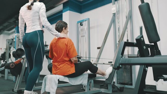 Personal trainer assisting senior woman with seated cable row exercise