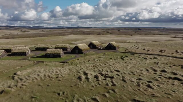 A group of traditional longhouses with turf-covered roofs nestled in a barren, rocky northern environment under a cloudy sky. This 3D environment represents a historic Scandinavian settlement or remot