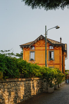 Yellow and orange old home on a cobblestone street with a vine covered wall next to it the village known as the balcony of the alps at the top of the bromate funicular in Lake Como, Italy 