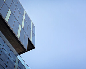 Obraz premium Modern glass building facade with geometric design against a clear blue sky, minimalist corporate architecture with negative copy space for professional business and real estate concepts.