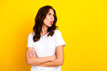 Obraz premium Young stylish woman in white tshirt with arms crossed making a playful tongue out expression against a bold yellow background