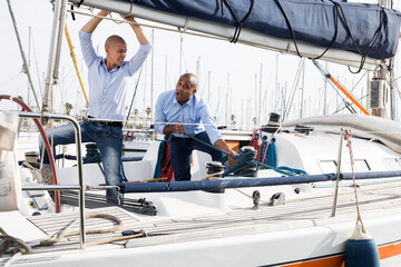 Two young men in blue shirts tidy up private sailing yacht in the seaport