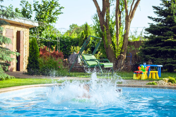 Splashing water after jumping. Kids play in swimming pool. Happy little boy with inflatable toy ring jumping into outdoor swimming pool.