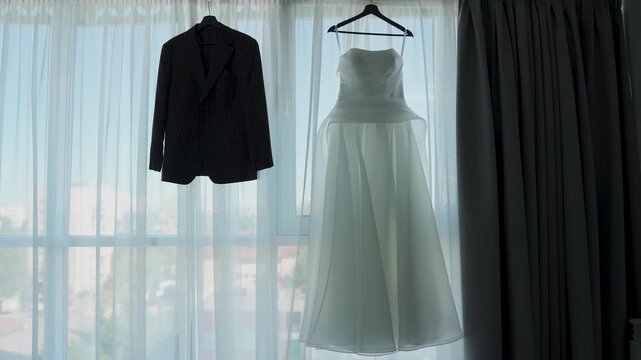 A wedding jacket and a wedding dress are hanging on the window