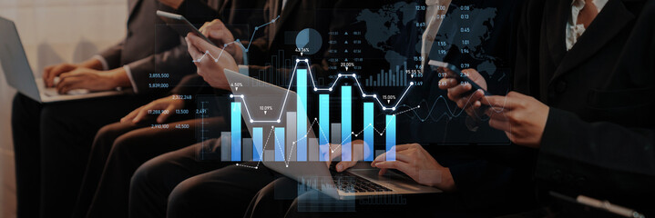 Group of business professionals engaged in a meeting, utilizing smartphones and laptops to analyze...