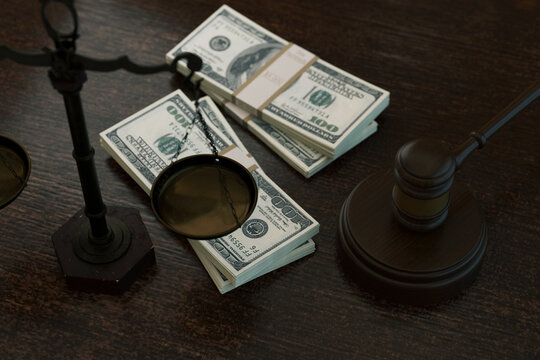 powerful conceptual shot featuring stacks of US hundred dollar bills balanced on legal scales next to a wooden judges gavel. Represents legal costs, corruption, bribery, and financial justice. Law