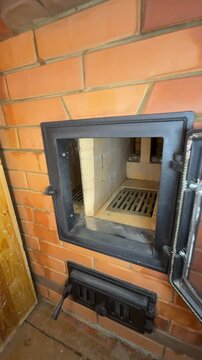 Man opening the stove's firebox door. Demonstrating the firebox made of fireclay brick and the stoves throat. Close-up. New brick heating stove. Construction of a wood-burning stove.