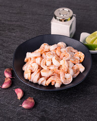 Uncooked orange shrimps in a black plate over stone background