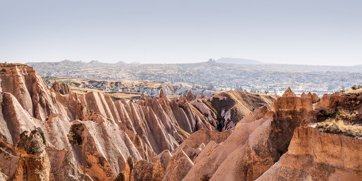 Panoramic view of the Red Valley (Kizilcukur Vadisi) stone formations sculpted by wind and erosion with Uchisar castle and Goreme town on the horizon. Sunny summer day in Cappadocia, Turkey.