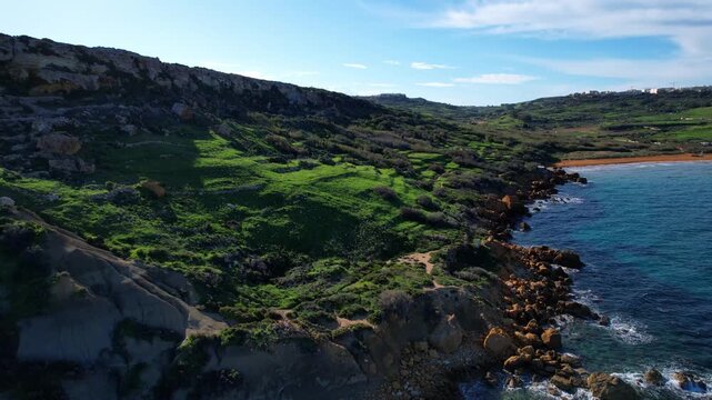 Aerial drone view of the most beautiful Malta beach in Gozo, vibrant red sand Ramla beach with crystal clear blue water and mesmerizing waves with lush green vegetation around it and the famous Mixta 