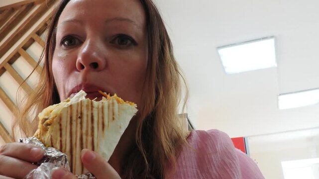 a woman sits and eats in a cafe. Female hand holding fresh tortilla wrapped. Gourmet concept. tasty chicken Doner kebab or shawarma. Vegetarian Tortilla wrap with falafel and salad, tacos. Junk food.