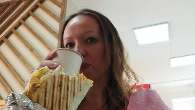 a woman sits and eats in a cafe. Female hand holding fresh tortilla wrapped. Gourmet concept. tasty chicken Doner kebab or shawarma. Vegetarian Tortilla wrap with falafel and salad, tacos. Junk food.