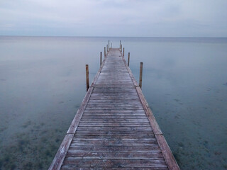 Obraz premium A weathered wooden pier stretches into the calm, hazy water under a grey sky. Denmark