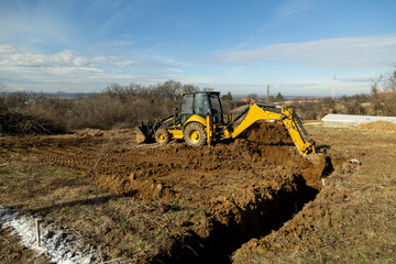 Backhoe excavator digging foundation trench on rural construction site