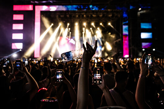 Crowd holding smartphones recording live music concert and throwing water bottle