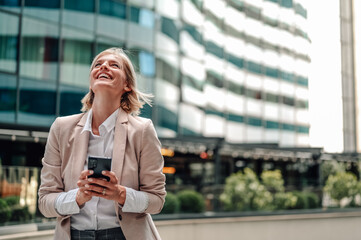 Fototapeta premium Businesswoman looking up smiling holding smartphone on city street