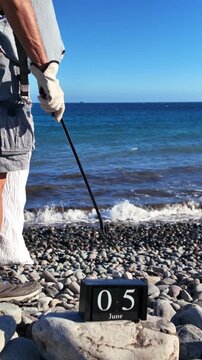 Unrecognizable ecological volunteer with a grabber and a bag cleaning up a polluted pebble beach during World Environment Day, a concept about taking action against climate change