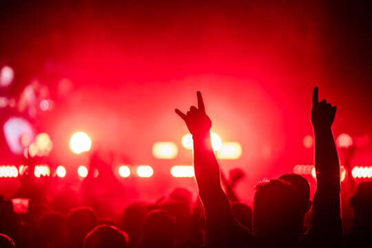 Audience raising hands and making rock and roll sign at concert with red lights