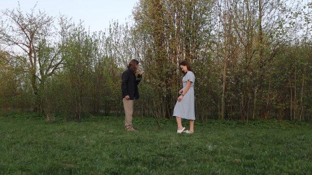 A loving couple in summer clothes walks through a summer park field in nature.v