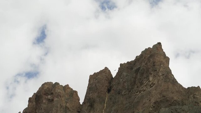 Andean condor soaring through a cloudy sky with rocky peaks of a mountain range in Patagonia
