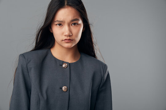 Portrait of serious young woman with long straight hair wearing dark buttoned jacket on gray background looking at camera with intense confident expression for professional style.