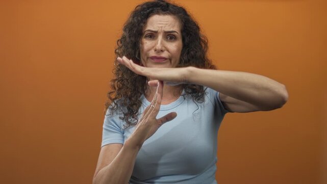 Woman wearing blue shirt frowning makes timeout gesture with hands in orange studio; pause break frustration.