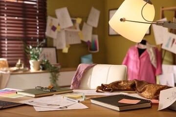 Fashion designer's workplace with sketches of outfits, stationery and fabric on wooden table indoors, closeup