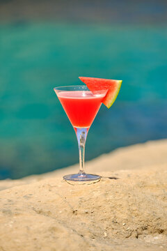 Watermelon cocktail in martini glass on rock overlooking sea