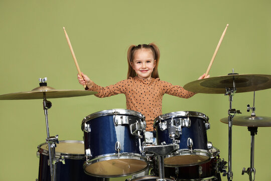 Little girl learning how to play drums on green background