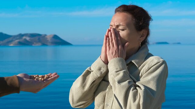 Woman refusing offered pistachios. Woman standing near seashore, repeatedly refusing offered pistachios with changing facial expressions, displaying clear signs of food rejection and aversion