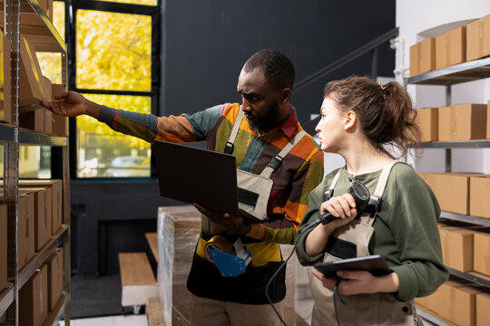 Multiethnic team using a scanner to check awb tags on stored goods, handling retail inventory for an e-commerce depot focused on small delivery. Order processing and distribution.