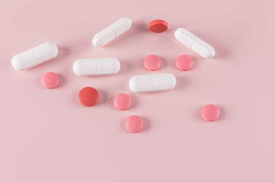 Assorted pills and capsules on pink background