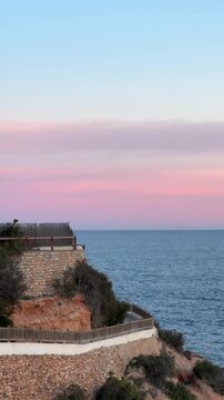 Pink color clouds above calm water on rocky coast. Beautiful sunset on Orihuela Costa, Alicante, Spain