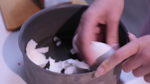 Woman's hands peeling hard-boiled egg over a pot