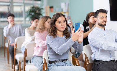 Obraz premium Female student takes pictures during a presentation at a lecture. Students sit in the classroom and scan the QR code to see all the training materials on the site.